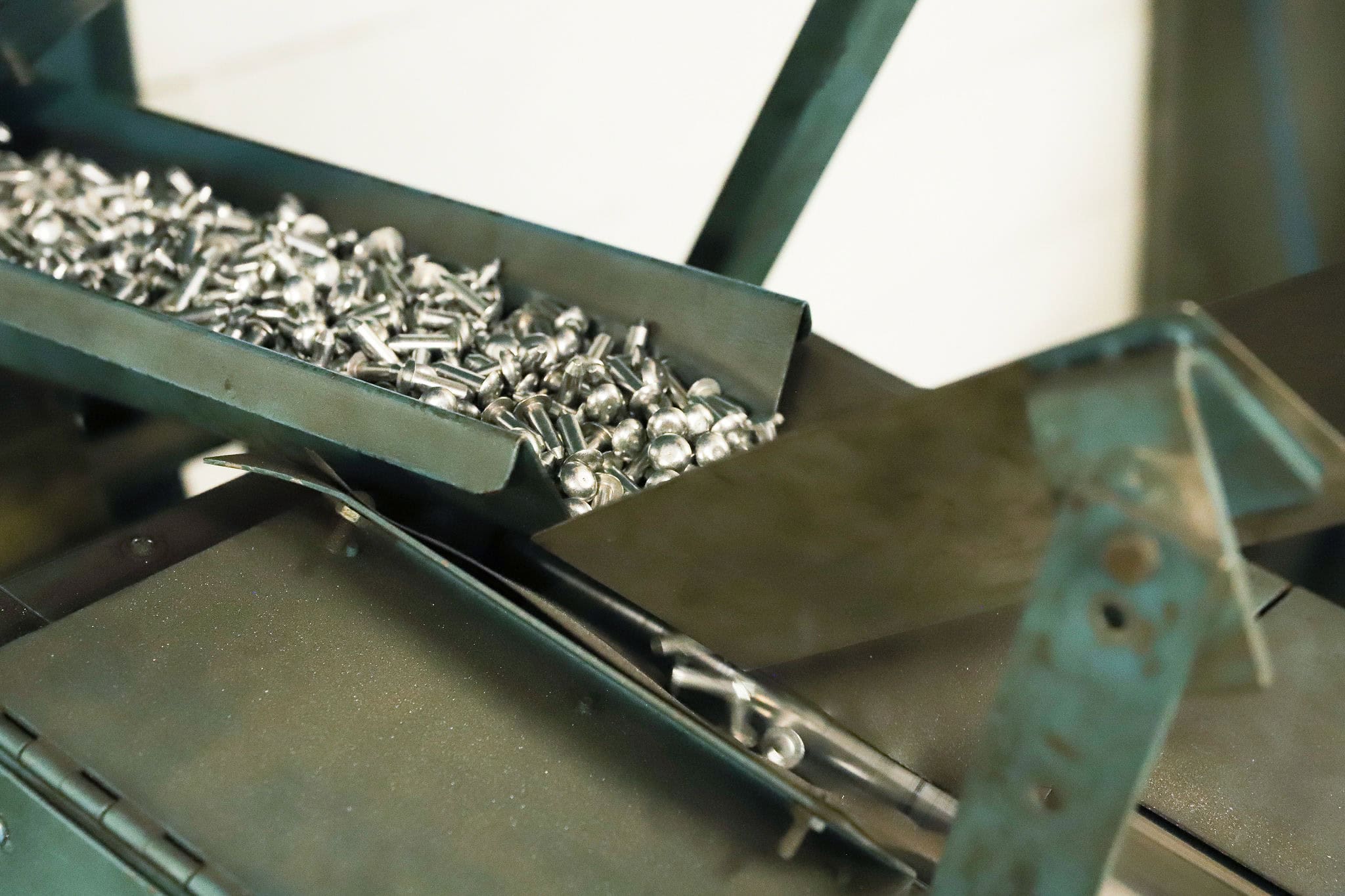 A metal tray filled with small metal parts, possibly machine components, moving along an industrial conveyor system.