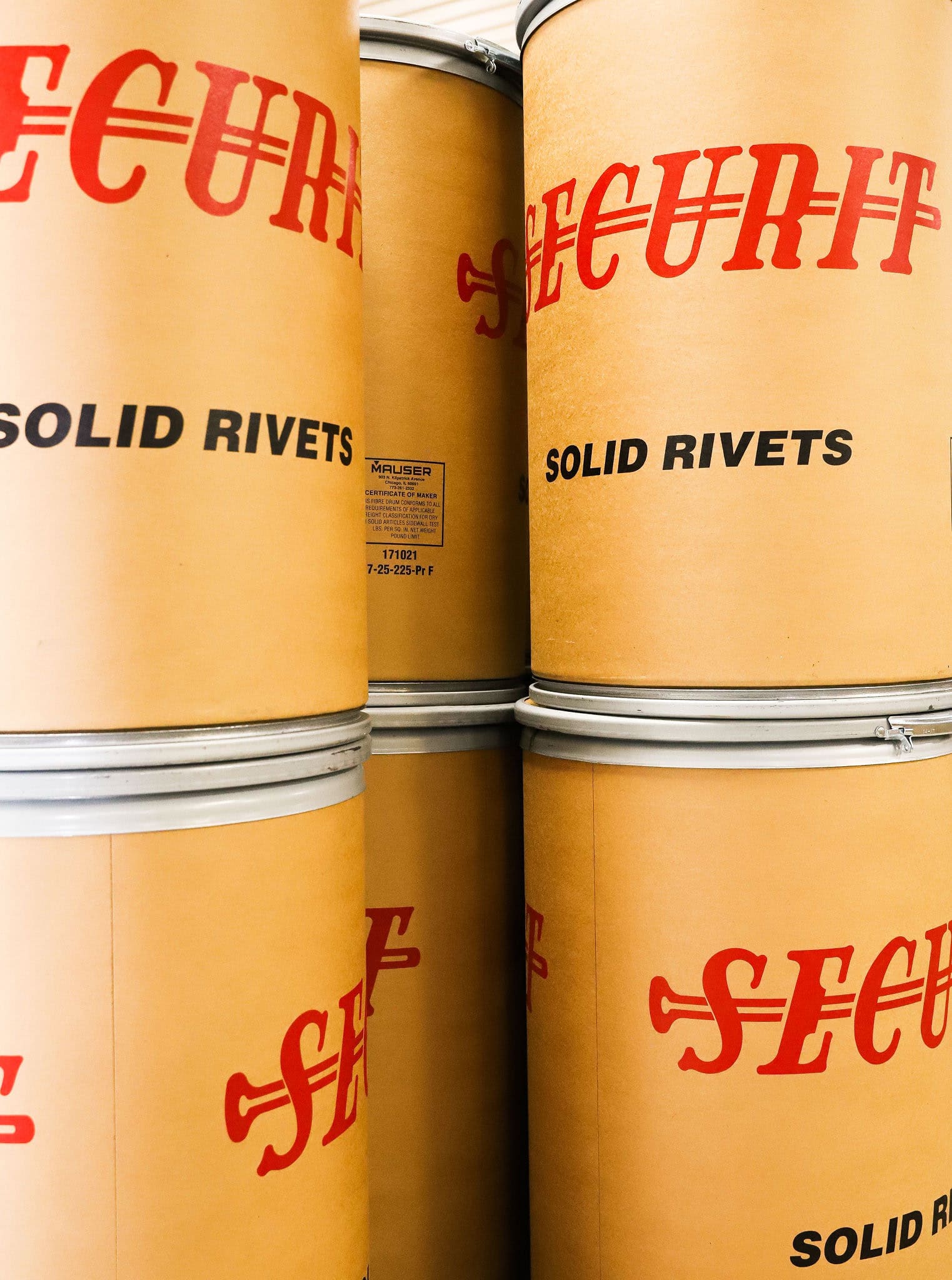 Large cylindrical containers labeled "SECURIT" and "SOLID RIVETS" are stacked closely together.
